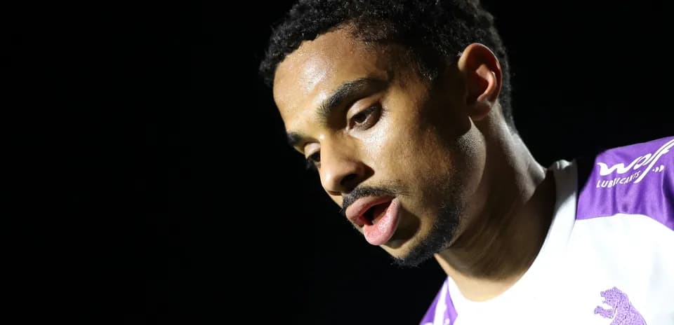 Jugador mirando hacia abajo con camiseta blanca y morada