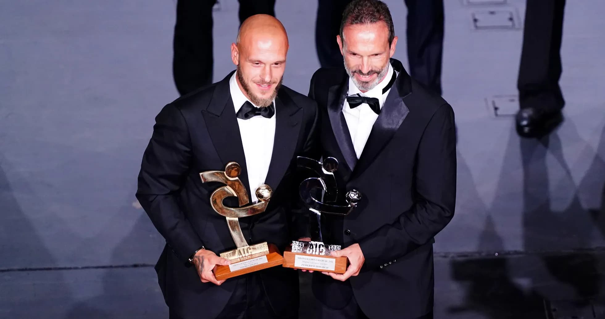 Dos hombres en traje sosteniendo trofeos en ceremonia
