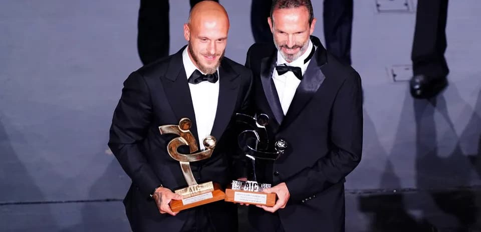 Dos hombres en traje sosteniendo trofeos en ceremonia