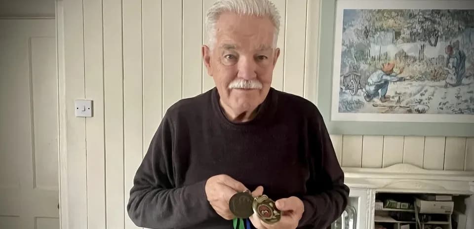 Hombre mayor sosteniendo medallas en su casa