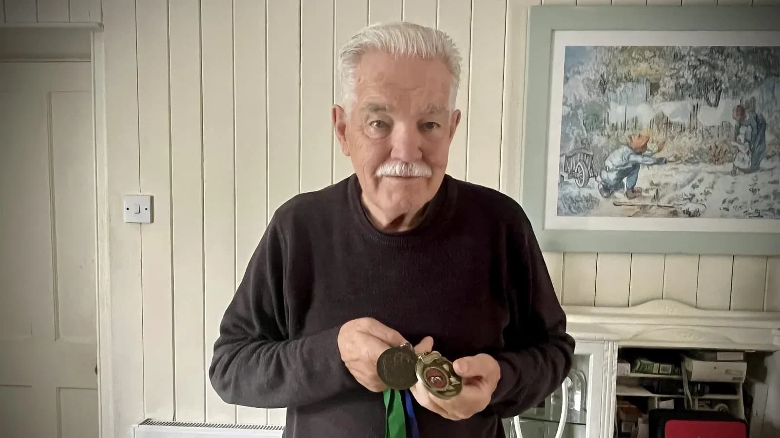 Hombre mayor sosteniendo medallas en su casa