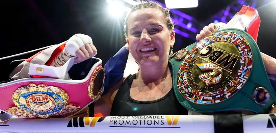 Boxeadora sosteniendo cinturones de campeona después de la pelea
