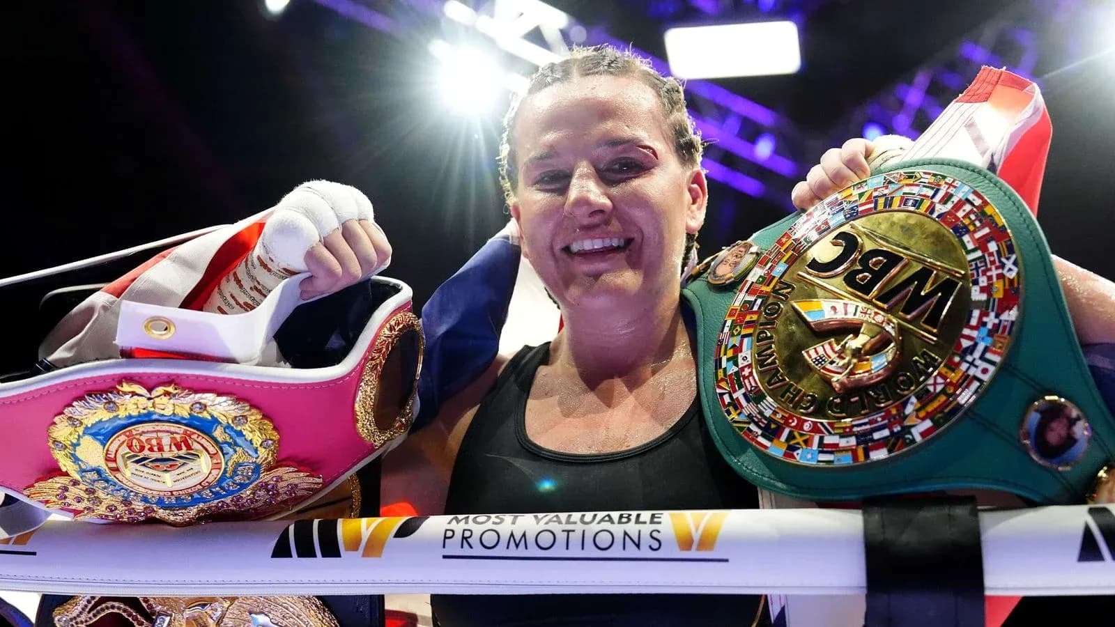 Boxeadora sosteniendo cinturones de campeona después de la pelea